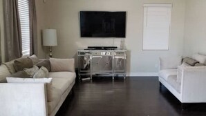 A living room with two white sofas, a flat-screen TV, a glass cabinet, and a window with blinds. - Charming 3-bedroom house in marvelous Phoenix with WiFi, AC (Phoenix)