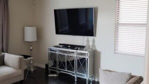 A living room with a sofa, a TV on a stand, a ceiling fan, and a window with blinds. - Charming 3-bedroom house in marvelous Phoenix with WiFi, AC (Phoenix)