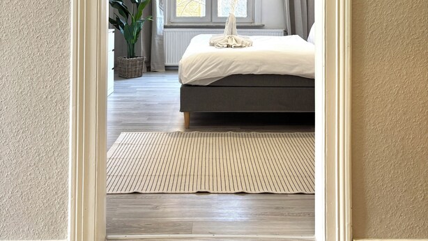 A bedroom with a bed, a large window, a hanging light fixture, and a view of the outdoors.
