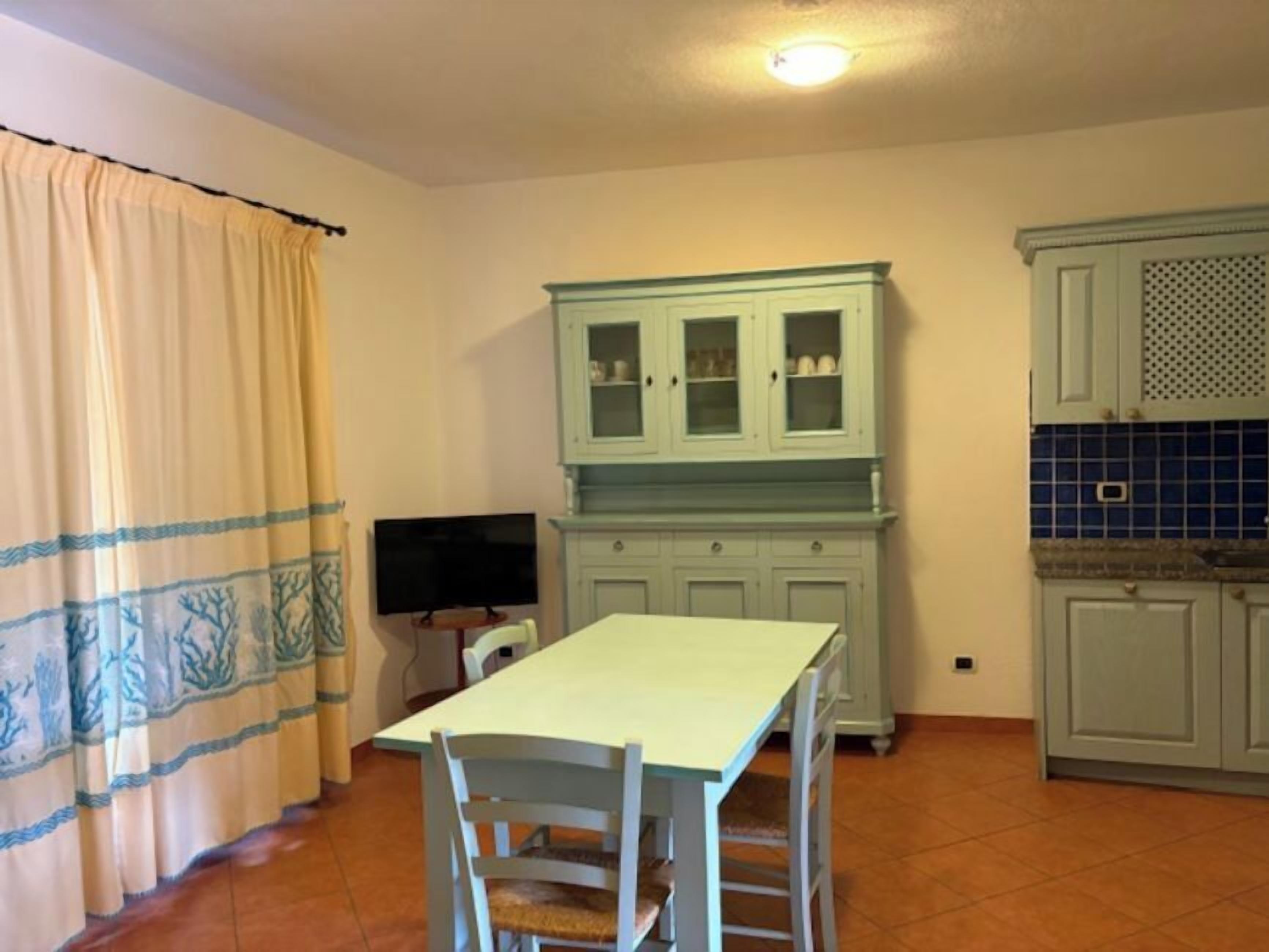 Una cocina con una mesa de comedor, sillas, un televisor y armarios.