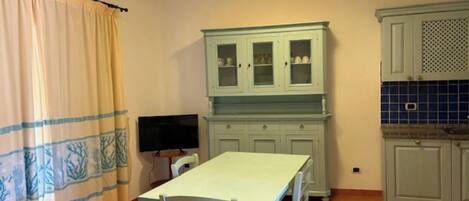 Una cocina con una mesa de comedor, sillas, un televisor y armarios.