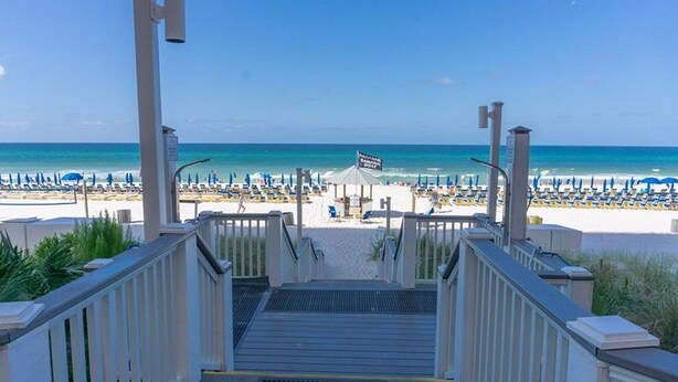 A beach view with a staircase leading to the beach, umbrellas, and a flag. - 3BR 2BA @ The Calypso Breathtaking View, Walk to Pier Park (Panama City Beach)