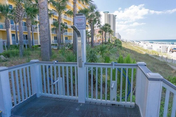 Une entrée fermée par un portail, avec une rampe métallique menant à un balcon d’où l’on a vue sur une plage.
