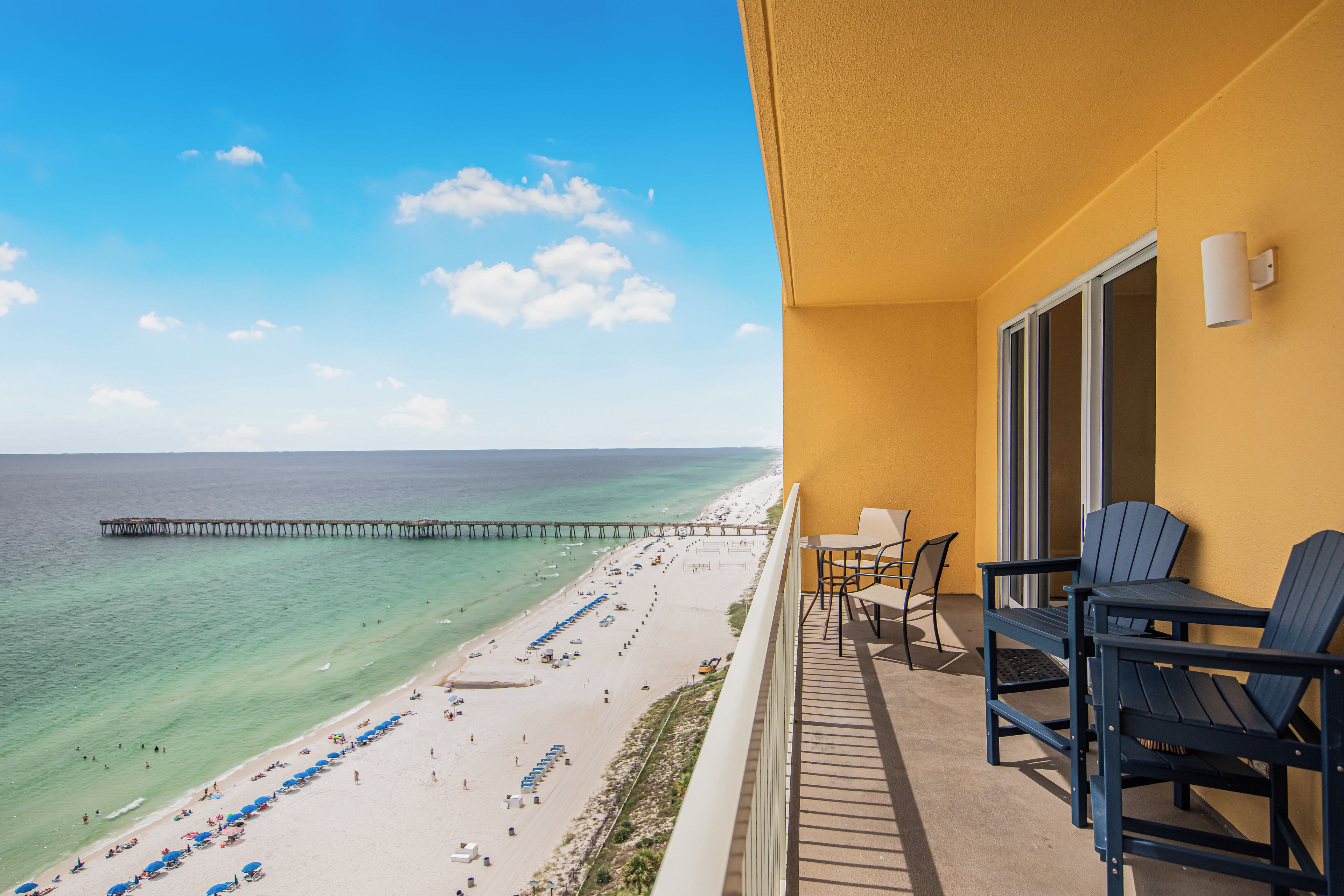 Un balcon avec vue sur une plage et une jetée, comprenant un espace salon extérieur et une porte.