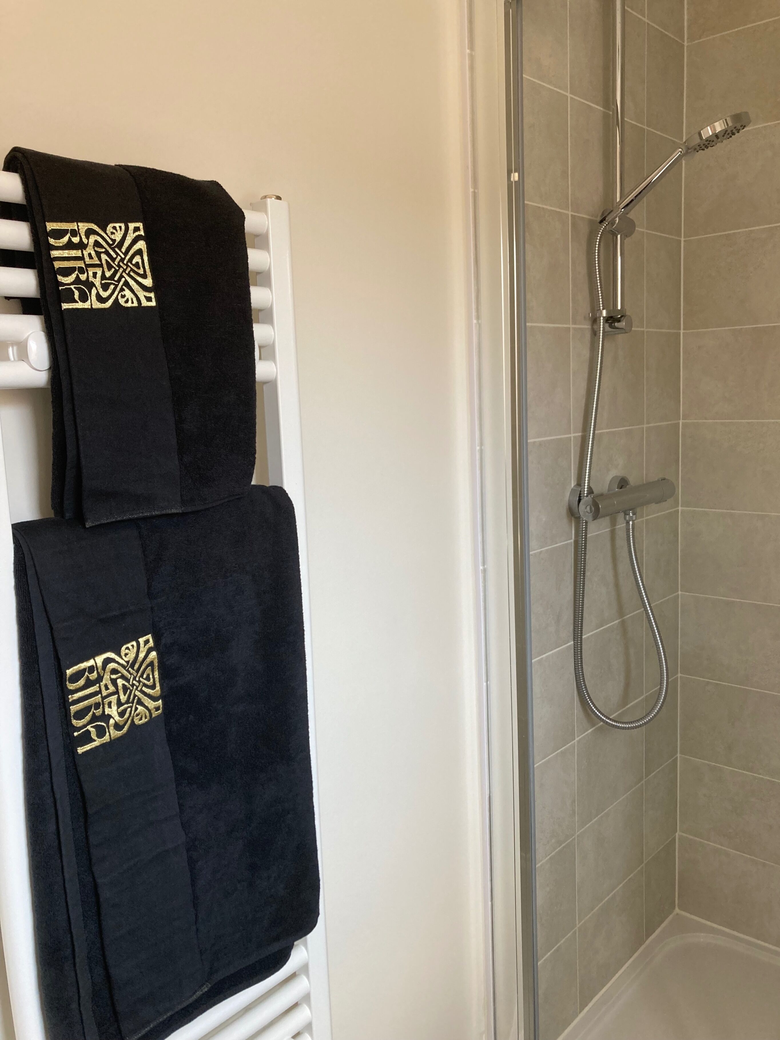 A bathroom with a shower, a towel rack with two towels, and a tiled wall.