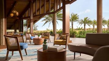 A spacious lounge area with comfortable seating, large windows, and a view of palm trees.