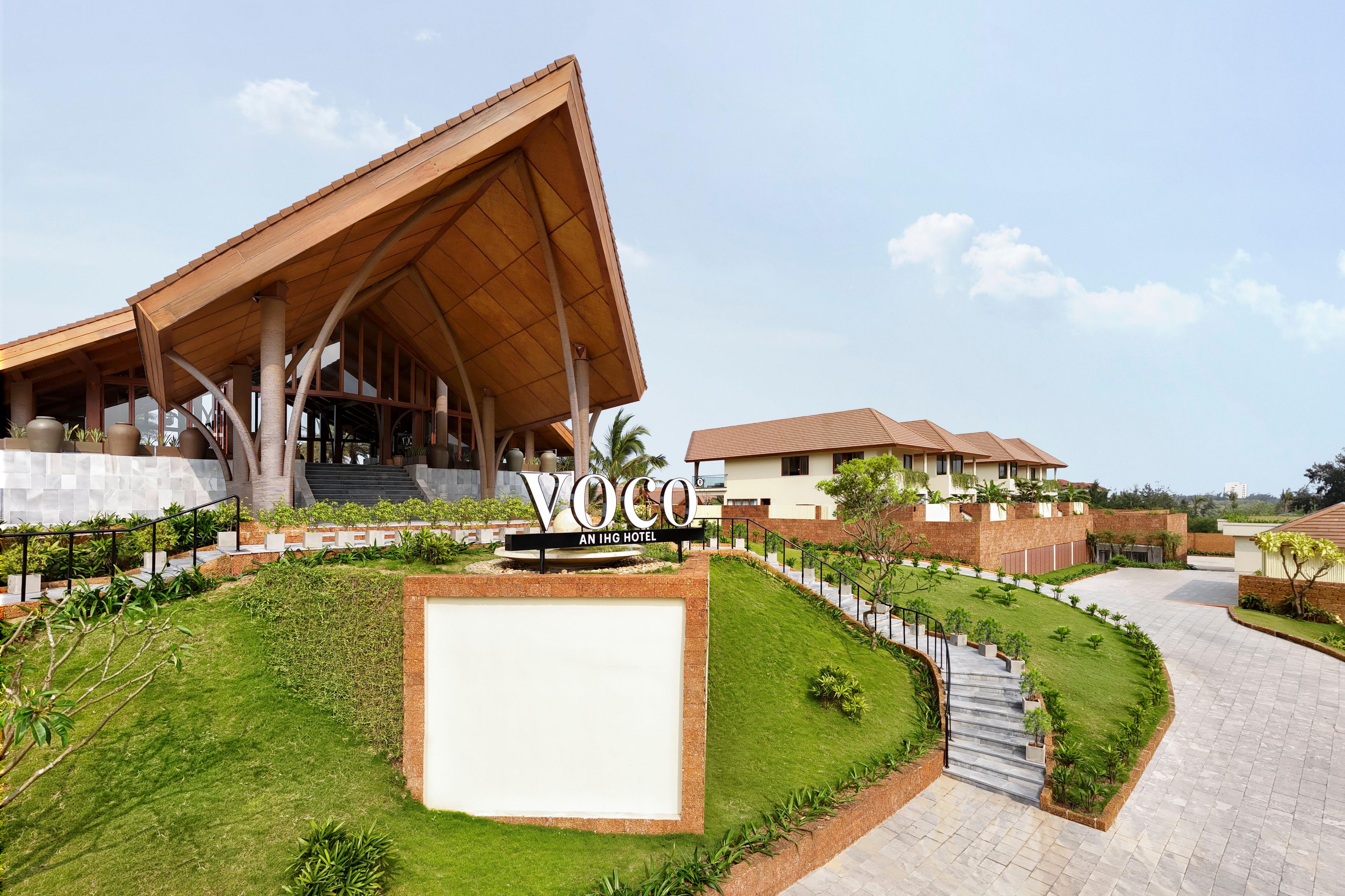 A modern hotel with a prominent wooden structure, a well-maintained lawn, and a clear sky.