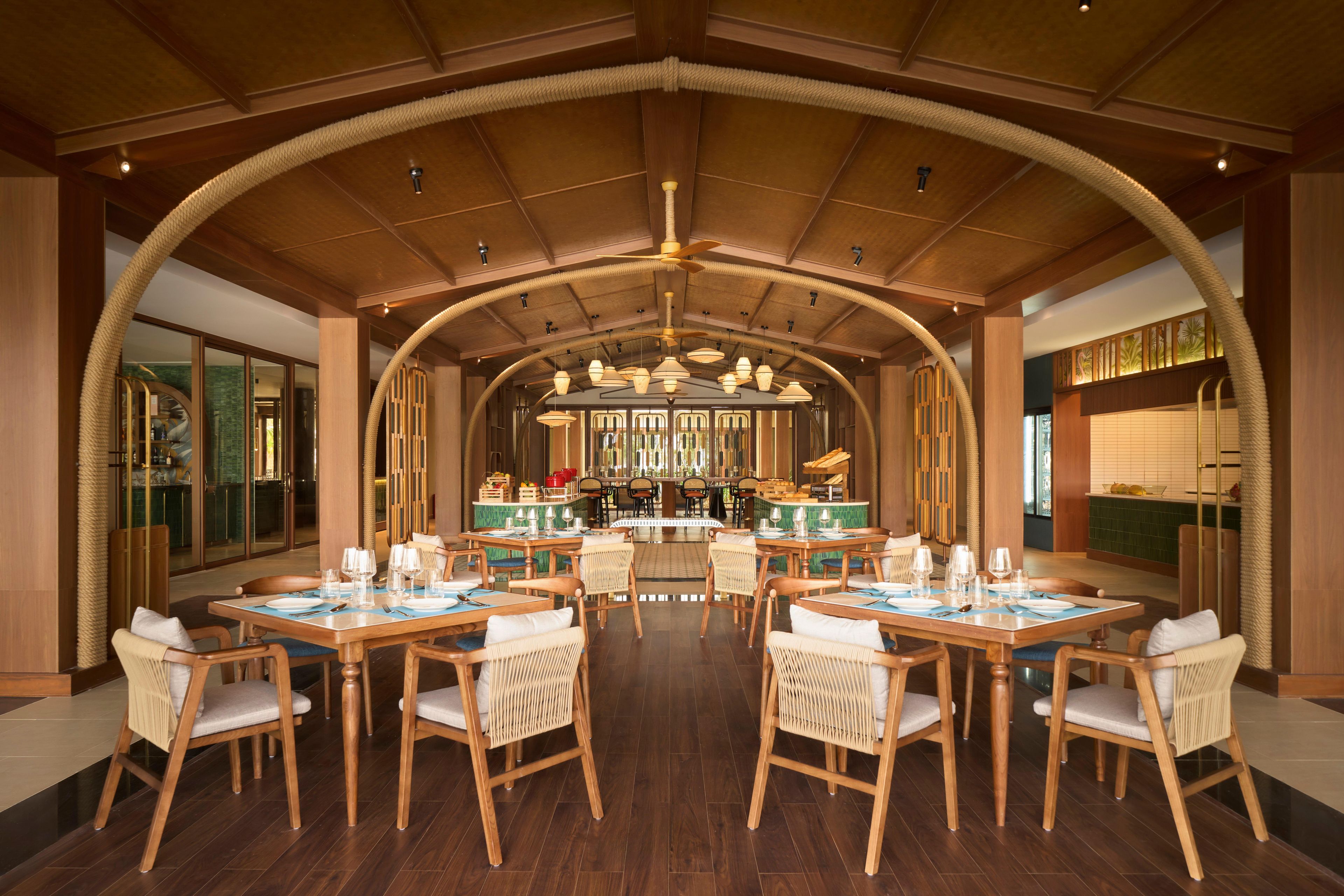 A spacious dining area with high wooden ceilings and a central bar. Tables are set with chairs and dining ware.
