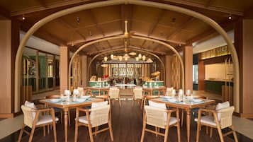 A spacious dining area with high wooden ceilings and a central bar. Tables are set with chairs and dining ware.