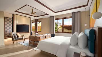 Quarto de hotel com uma cama grande, escrivaninha, cadeira, televisão e vista para o exterior.