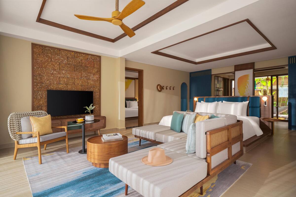 Una habitación de hotel moderna con una televisión de pantalla plana, un sofá, una cama, un ventilador de techo y vistas al exterior.