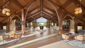 A spacious lobby with high ceilings, wooden beams, and a central seating area with rattan chairs and a large vase.