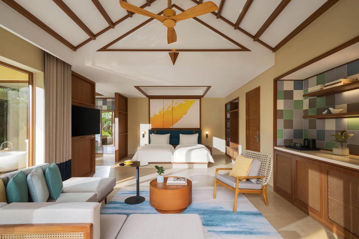 A modern hotel room with a large bed, a sofa, a dining area, and a ceiling fan.
