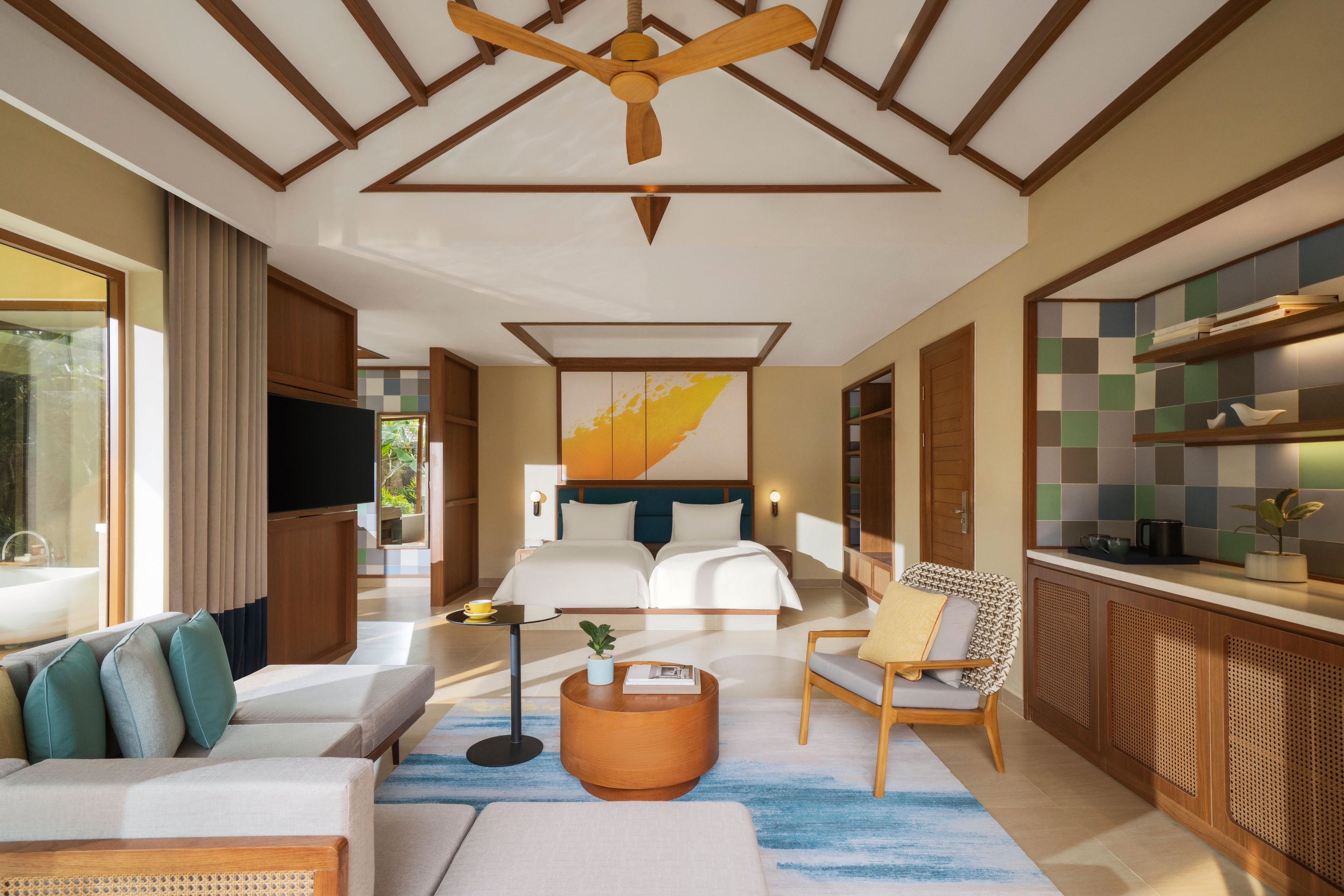 A modern hotel room with a large bed, a sofa, a dining area, and a ceiling fan.