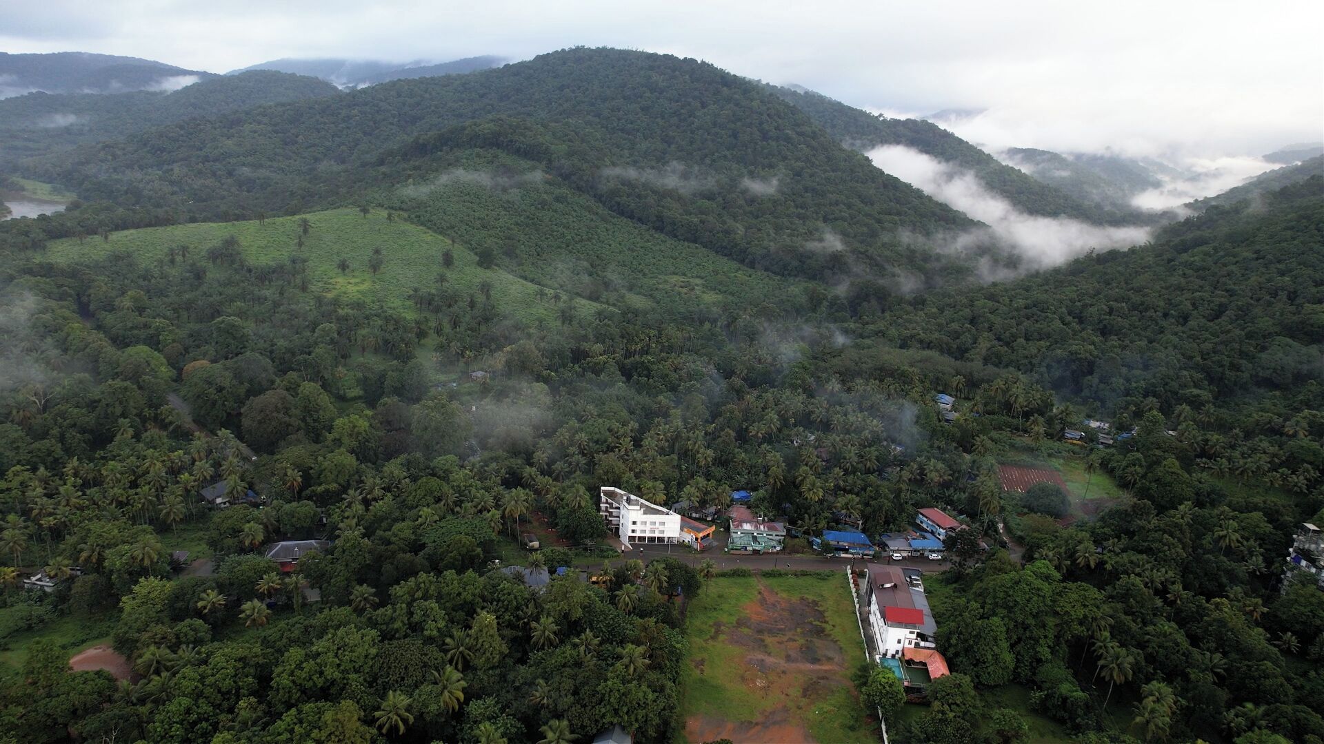 An aerial view of a resort with multiple buildings, surrounded by lush greenery and hills.