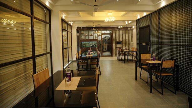 A modern dining area with tables and chairs, a ceiling fan, and a view into another room. - Sreeja Myst (Chalakudy)