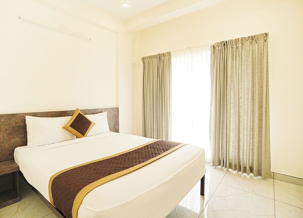 A neatly made bed with a quilted blanket and pillows, a headboard, and a window with curtains.