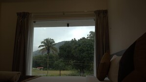 A hotel room with a large window, a bed, and a view of a palm tree and greenery. - Sreeja Myst (Chalakudy)