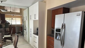 Una cocina moderna con armarios blancos, un refrigerador de acero inoxidable y un comedor con sillas de mimbre.