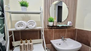 A bathroom with a white toilet, a white sink, a towel rack with towels, a small potted plant, and a mirror.