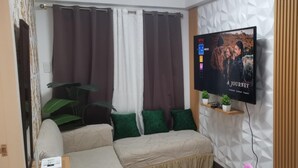 A modern living room with a sofa, green cushions, a TV on the wall, and a plant on a shelf.