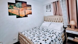 A bedroom with a bed, a nightstand, a lamp, a ceiling light, and wall art.