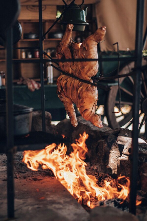 A large, roasted pig hanging over a fire, likely in a rustic kitchen setting.