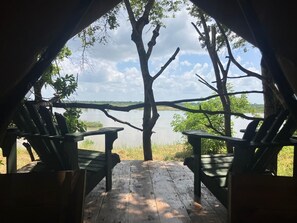 An outdoor seating area with wooden chairs and a view of a lake. - Rufiji Explorers (Mibuyusaba)
