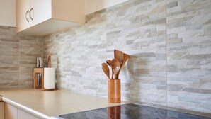 A kitchen with a stone backsplash, wooden utensils in a holder, and a stainless steel range hood.
