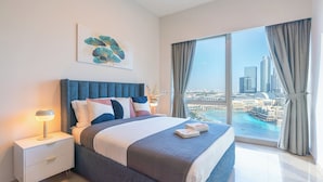 Una camera da letto moderna con un grande letto, un comodino, una lampada e vista sulla città attraverso ampie finestre.