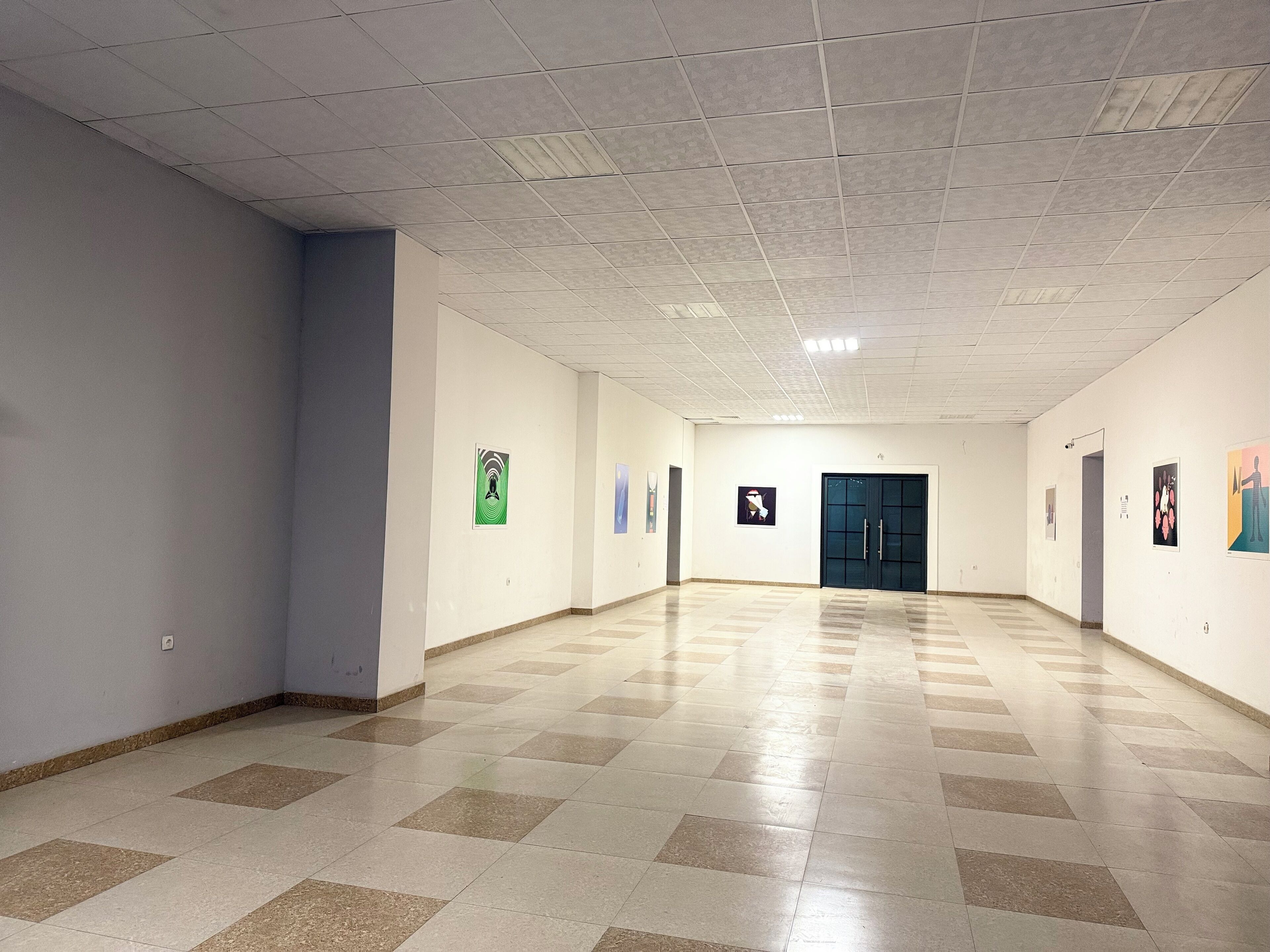 A spacious hallway with a tiled floor and white walls, featuring several doors and framed artwork on the walls.