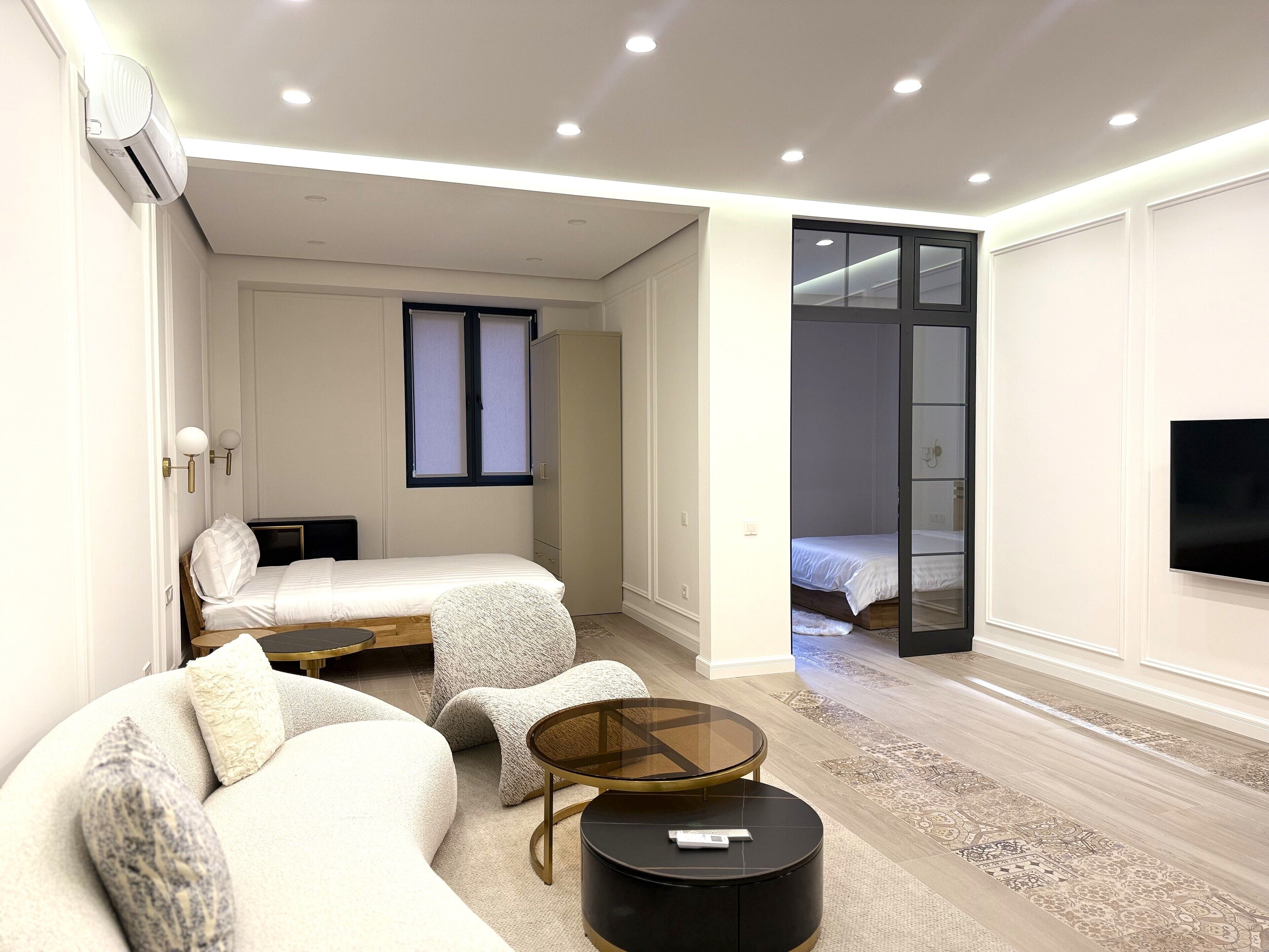 A modern, well-lit bedroom with a bed, a sofa, a small table, and a TV.