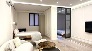 A modern, well-lit bedroom with a bed, a sofa, a small table, and a TV.