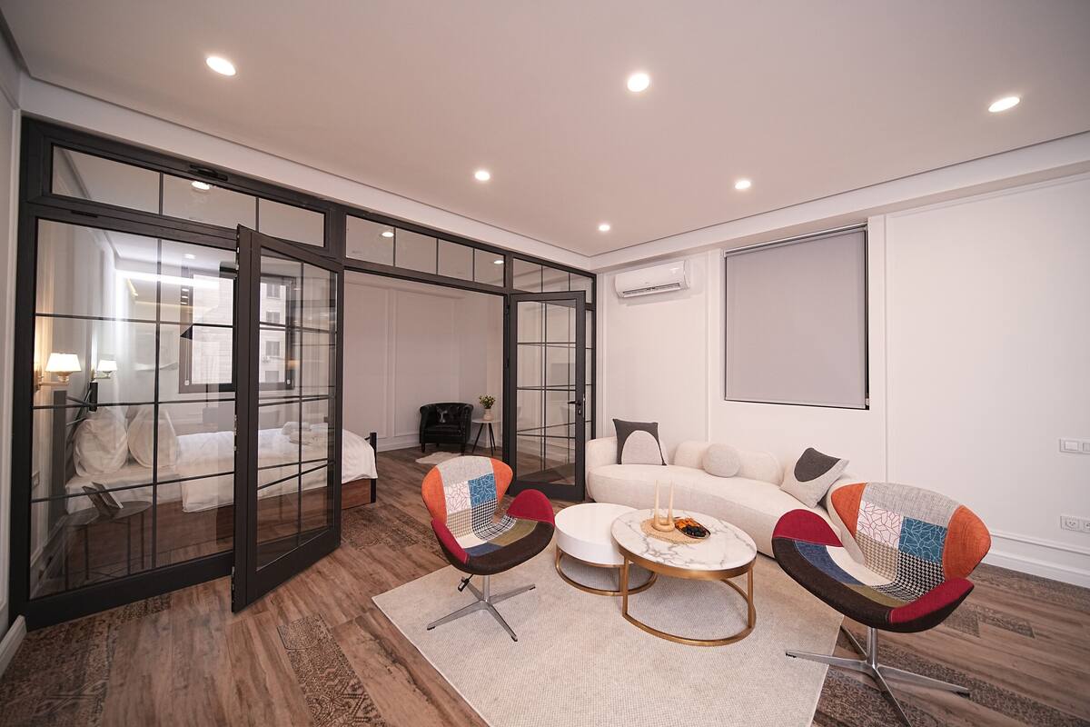 A modern living room with a glass partition, a sofa, two chairs, and a round coffee table.
