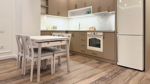 A compact kitchen with a dining table and chairs, a built-in oven, and a refrigerator. - Sweet Home Prime Apart-Hotel (Yerevan)