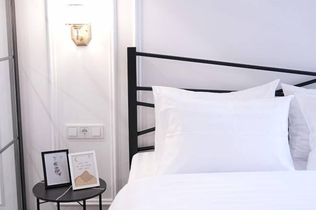 A neatly made bed with white bedding, a black metal headboard, and a small bedside table with framed artwork.