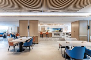 A modern dining area with tables and chairs, a kitchen in the background, and a view of the city. - Holiday Inn Express Haikou World Trade Center (Haikou)