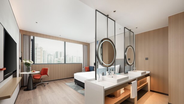 A modern hotel room with a large bed, a desk with a chair, a vanity with two sinks, and a large window offering a city view. - Holiday Inn Express Haikou World Trade Center (Haikou)