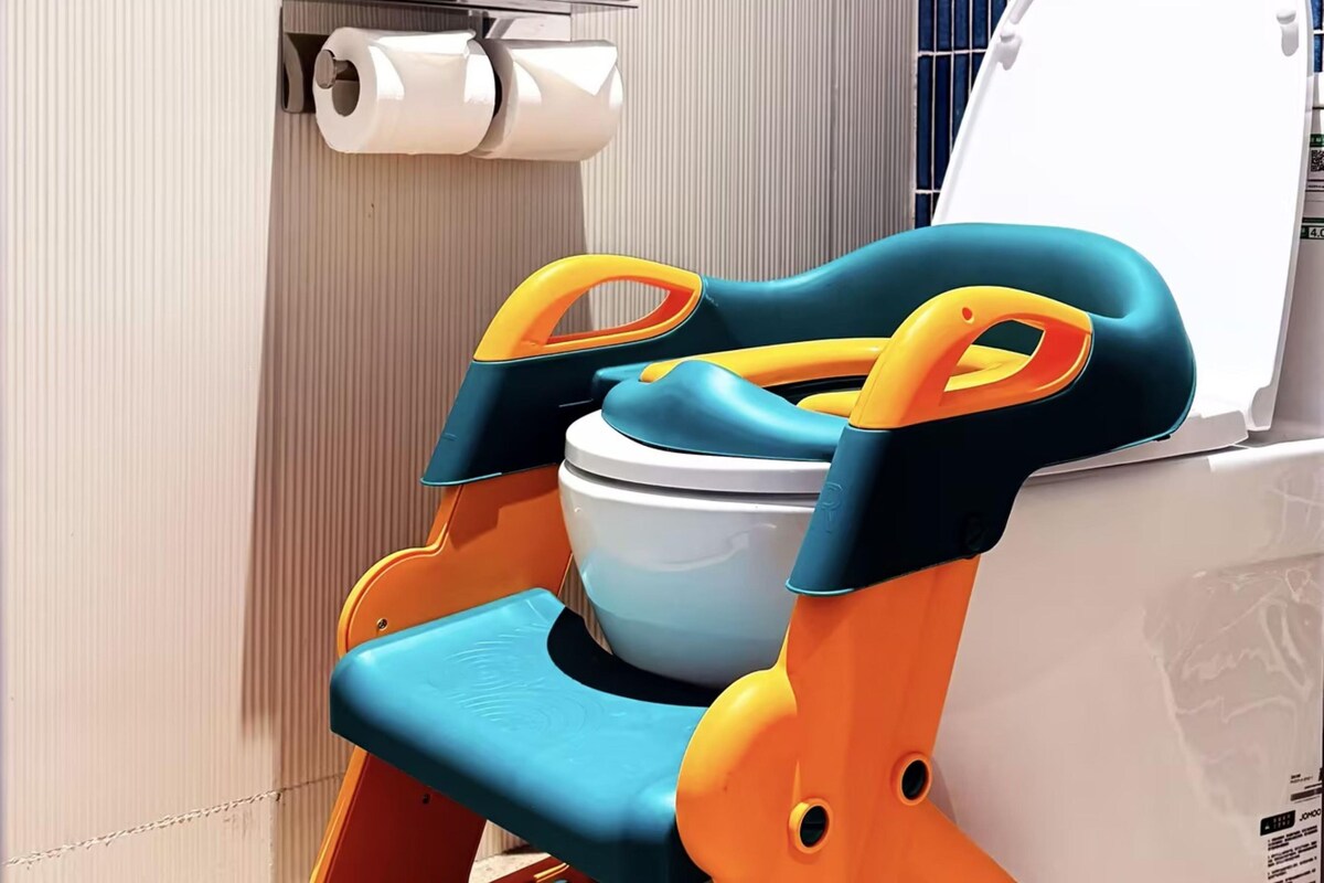 A bathroom with a toilet, a toilet paper holder, and a colorful step stool.