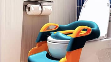Un baño con inodoro, dispensador de papel higiénico y un taburete pequeño de colores.