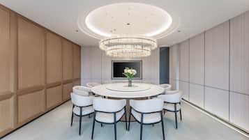 A modern dining area with a round table, eight chairs, a chandelier, and a flat-screen TV on the wall.