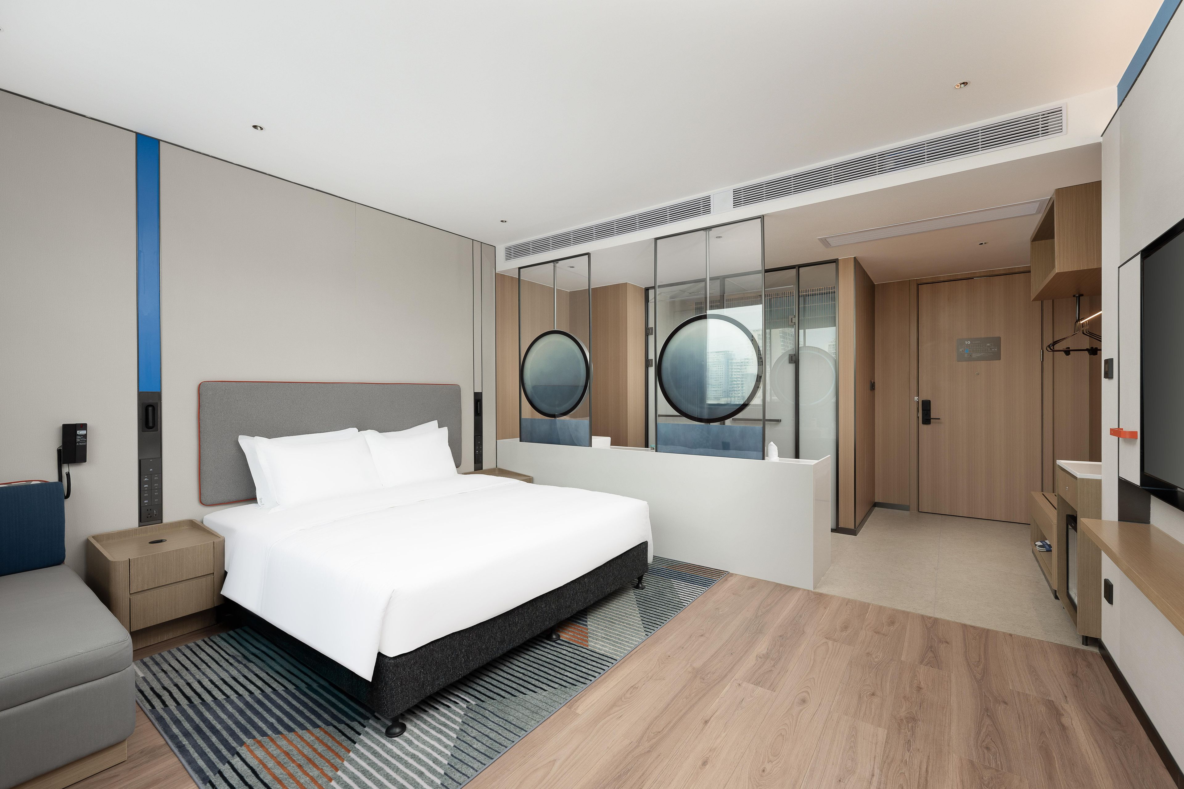 Een moderne hotelkamer met een groot bed, een nachtkastje, een garderobe, een spiegel en een televisie.