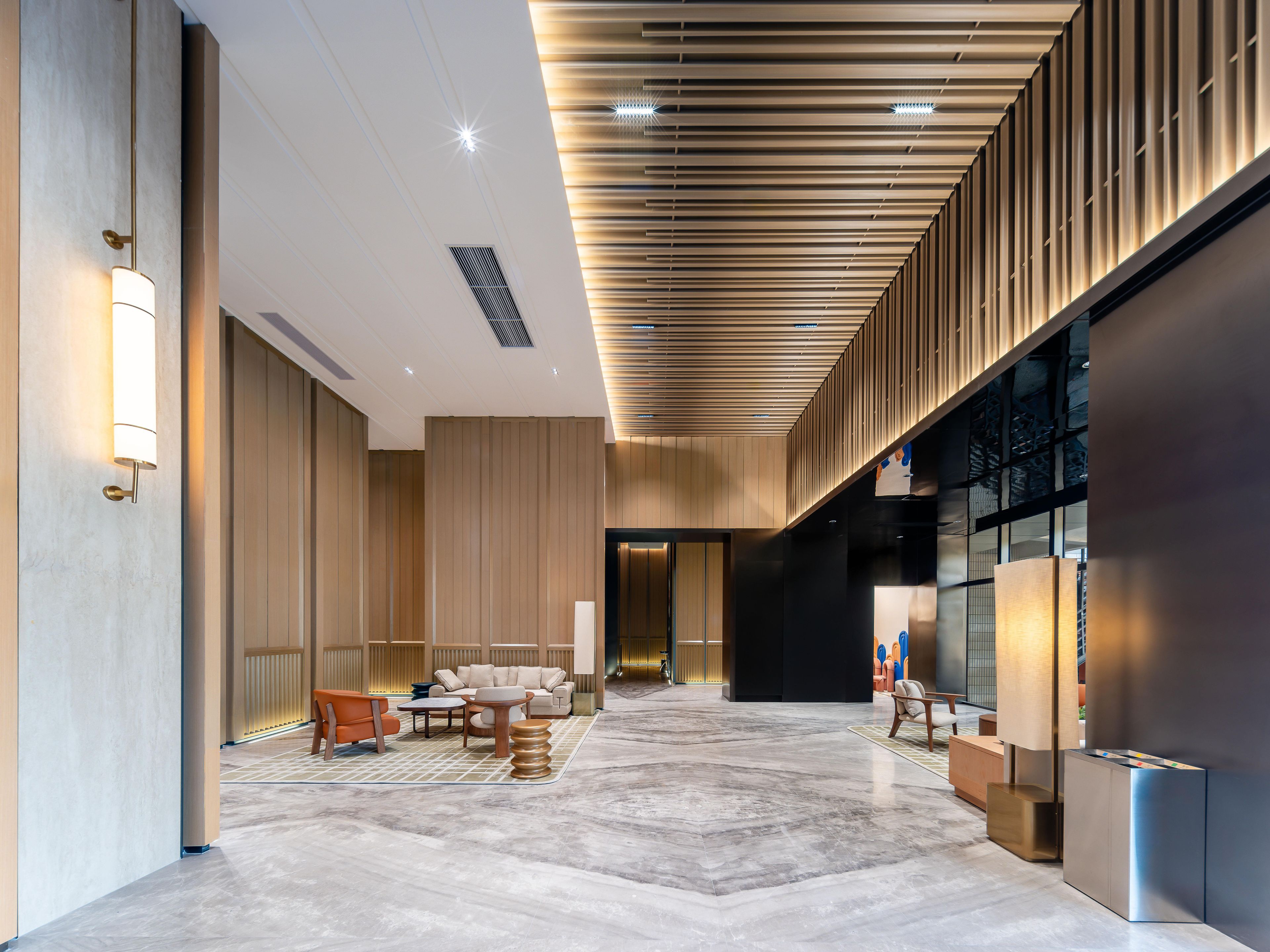 A spacious lobby with a modern design, featuring a seating area with sofas and tables, a large mirror, and a reception desk.