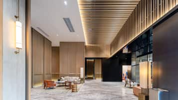 A spacious lobby with a modern design, featuring a seating area with sofas and tables, a large mirror, and a reception desk.