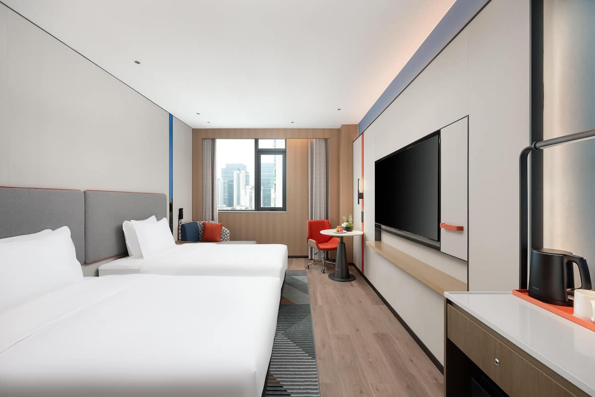 Habitación de hotel con dos camas, un escritorio, televisión y vista a la ciudad.
