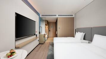 Una habitación de hotel moderna con televisión de pantalla plana, una cama, una mesita de noche y una pequeña área con kitchenette.