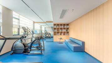 Un gimnasio moderno con equipo de ejercicio, piso azul, una estantería y un área de descanso.