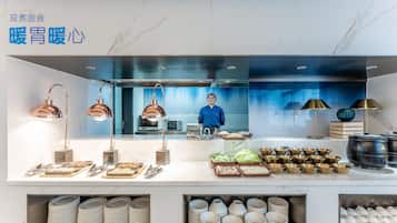A buffet setup with various food items and utensils, a person in the background, and a modern kitchen area.
