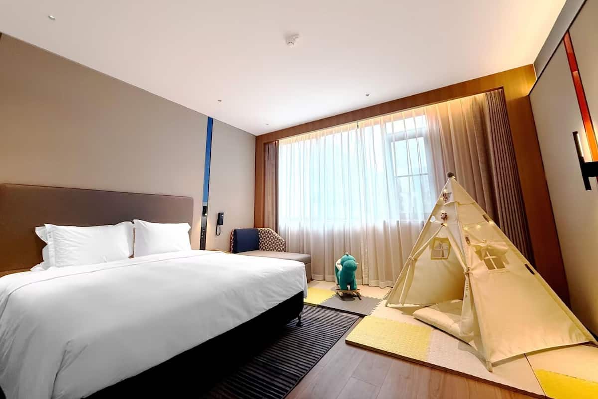 Habitación de hotel con una cama grande, un rincón de descanso, una estructura similar a una tienda de campaña y un amplio ventanal con cortinas.