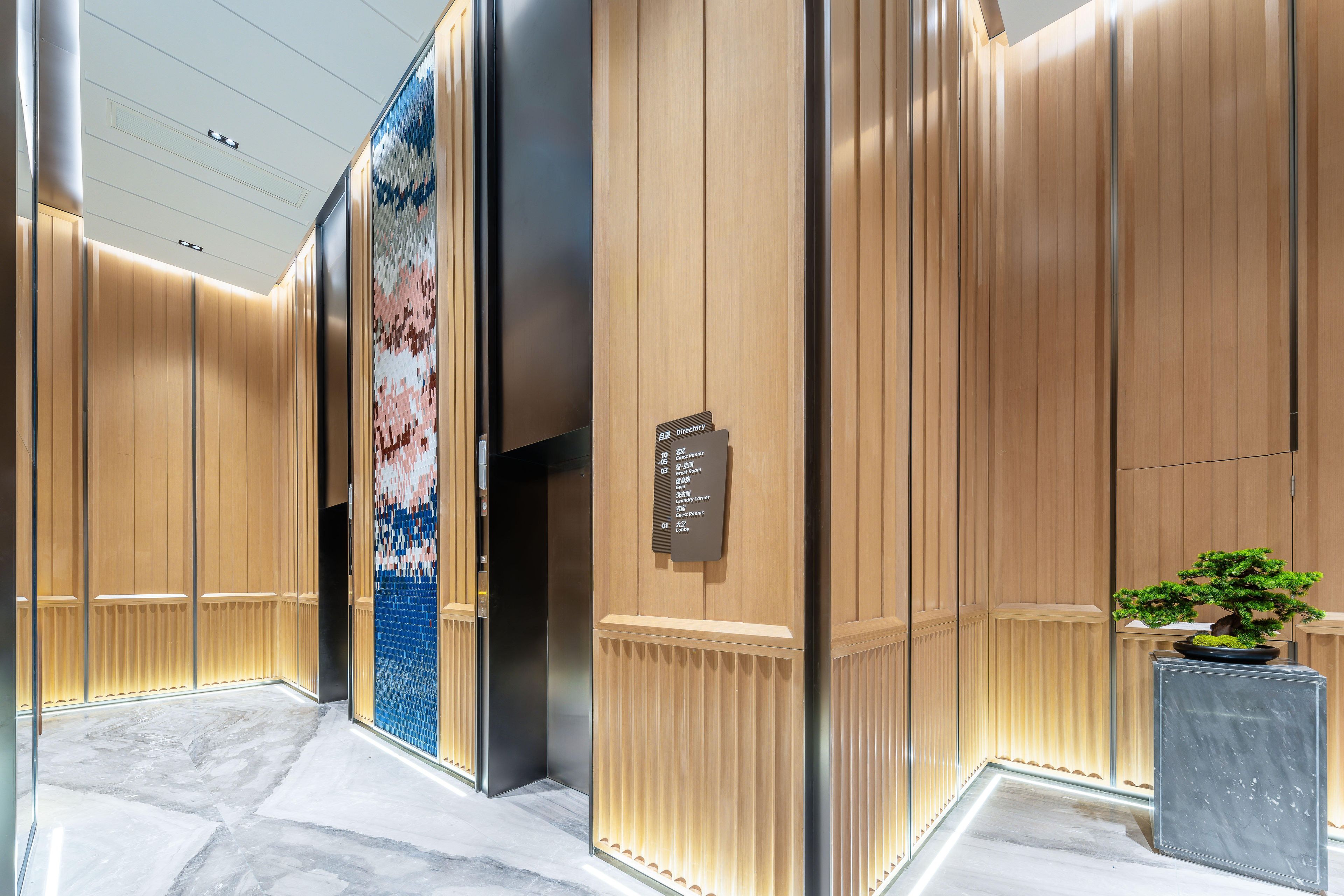 A modern elevator interior with a directory sign, wooden paneling, and a potted plant.